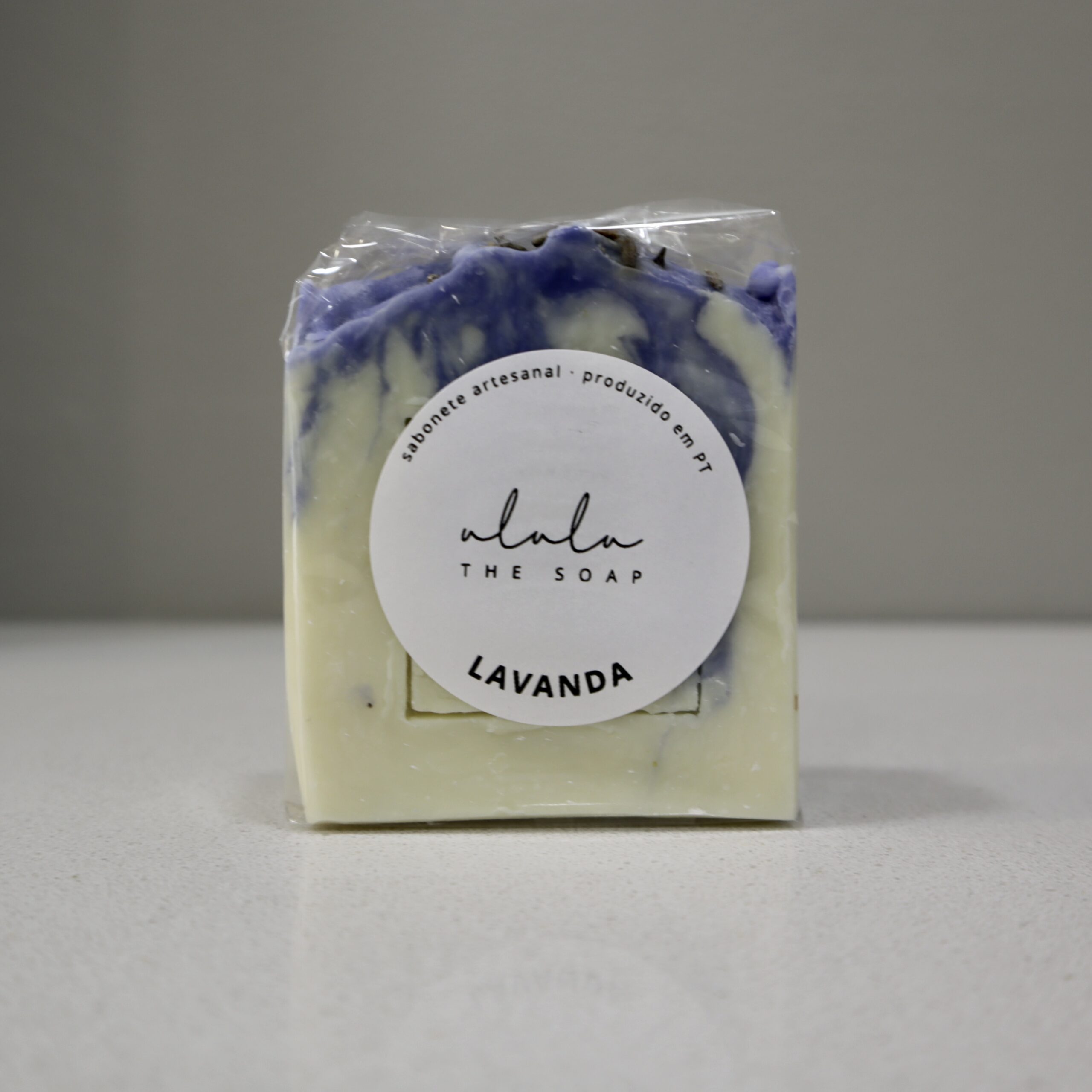 Sabonete artesanal de lavanda embalado em invólucro transparente com etiqueta identificativa e aparência delicadamente floral.